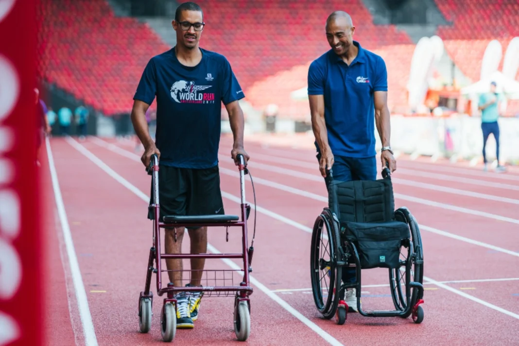 Man using a walking frame beside a wheelchair on an athletics track during rehabilitation training